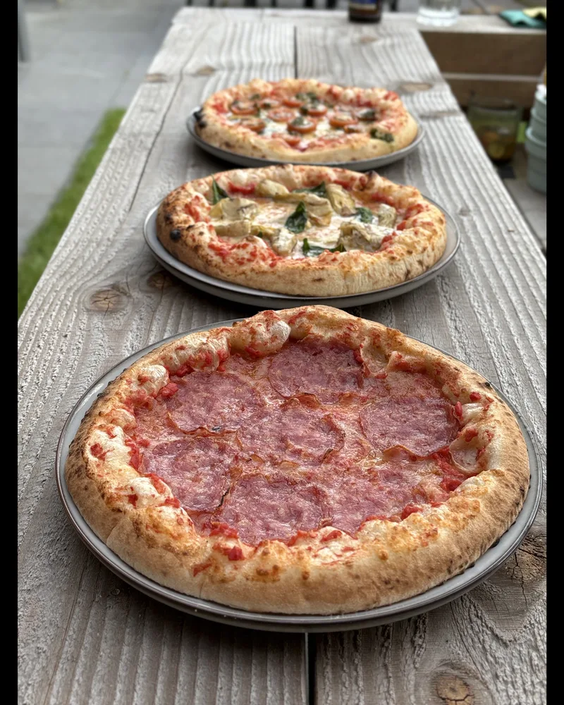 Drie vers gebakken pizza's op borden in een rij op een houten tafel buiten