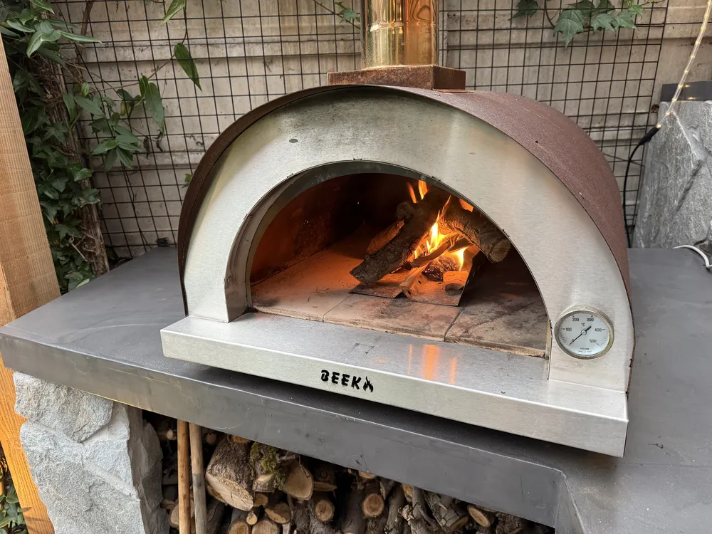 Houtvuur brandt achterin de RVS pizzaoven met thermometer, buiten op een betonnen werkblad