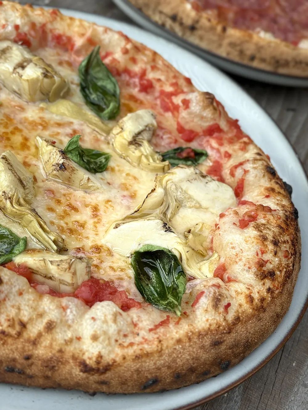Close-up van een vers gebakken pizza met artisjok, mozzarella en basilicum op een bord