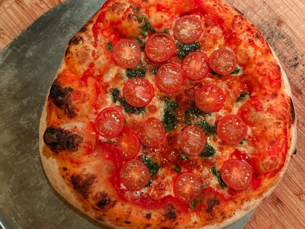 Vers gebakken pizza met tomatensaus, cherrytomaten en kruiden op een houten snijplank